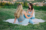 Ich sitze mit einer Klientin auf einer Picknick Decke und sehen uns gegenseitig an. Im Hintergrund sieht man die Natur, wir sitzen auf der Wiese. So kann coaching auch sein - draußen in der Natur.
