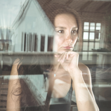 Nachdenkliche Frau blickt durch ein Fenster, ihre Hand stützt das Kinn – Symbolbild für Selbstreflexion und psychologische Beratung bei emotionaler Belastung.