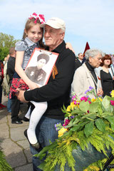 Großvater mit Enkelin auf dem Arm, mit Foto eines Soldaten der Roten Armee.  Sowjet. Ehrenmal Treptower Park Berlin. Foto: Helga Karl am 9. Mai 2015