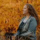 Susanne Kruse sitzt ruhig in herbstlicher Natur, mit weichem Blick zur Seite. Eine Haltung von Klarheit und Ankommen.