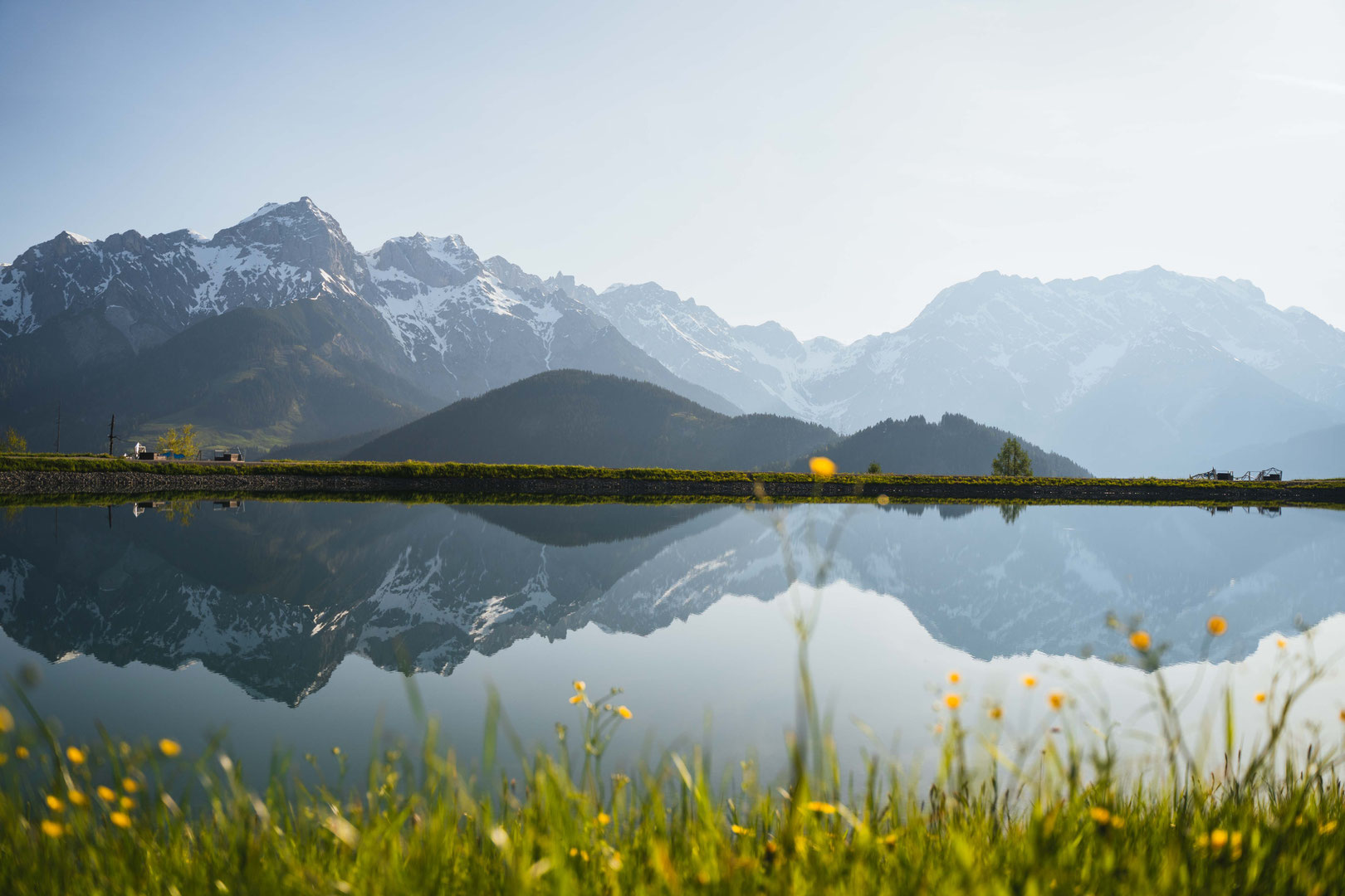 Panoramic view of the Hochkönig massif, reflected in the natural swimming pond at the Hochkönigin Wellness Hotel in Maria Alm, Salzburg