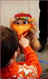 A colorful Puppets Please bird nibbles playfully on a child's finger