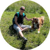 Tamara mit braun-weißem Hund in Wiese sitzend.