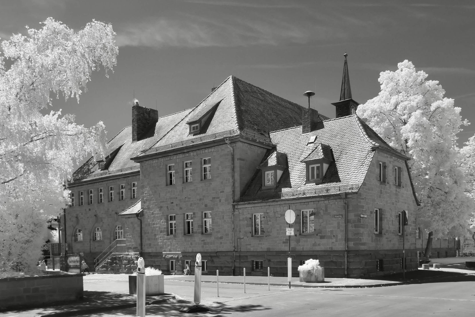 Das Gebäude der Schule in Zeil am Main zeigt sich als stattliches, mehrstöckiges Bauwerk mit traditioneller Architektur und kleinem Turm. Die Schwarz-Weiß-Infrarotaufnahme lässt die Bäume leuchtend weiß erscheinen.