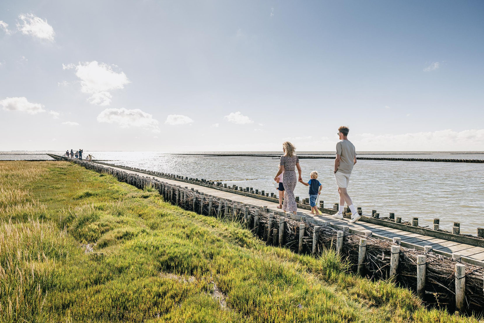 Familien gehen auf Holzsteg zwischen Salzwiesen und Nordsee