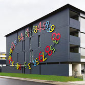 Wall installation by Paolo Grassi in Cadenazzo, vibrant numeric composition on black building facade, site-specific artwork.
