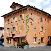 Site-specific facade intervention by Paolo Grassi for Bad Ragartz Triennale, colorful numeric installation on peach-colored building.