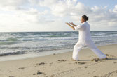 Un homme en kimono blanc pratique le Tai Chi sur une plage