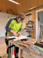 Auszubildender fertigt Nussbaum-Holzfedern zur Stabilisierung von Rissen in einer massiven Eschenbohle für eine individuelle Outdoor-Küche nach Maß