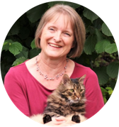 Lachende Astrid Huber mit magentafarbenen T-Shirt und braun-schwarzer Tigerkater Rico auf ihrem Schoß. Grünpflanzen im Hintergrund.