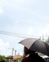 道路では暑さを避けるため、日傘を差して歩く人の姿も=26日