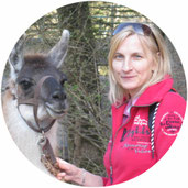 Teilnehmerin bei Tierkommunikation Seminar weiß-grauem Lama. Hintergrund Wald.