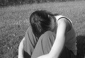 Frau auf Wiese mit Kopf auf Knien, traurig, erschöpft