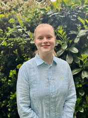Portraitfoto von Jolina Hukemann in Bluse vor grüner Hecke.