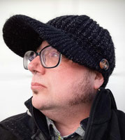Photograph of a white man with muttonchops, glasses, and a black knit cap.