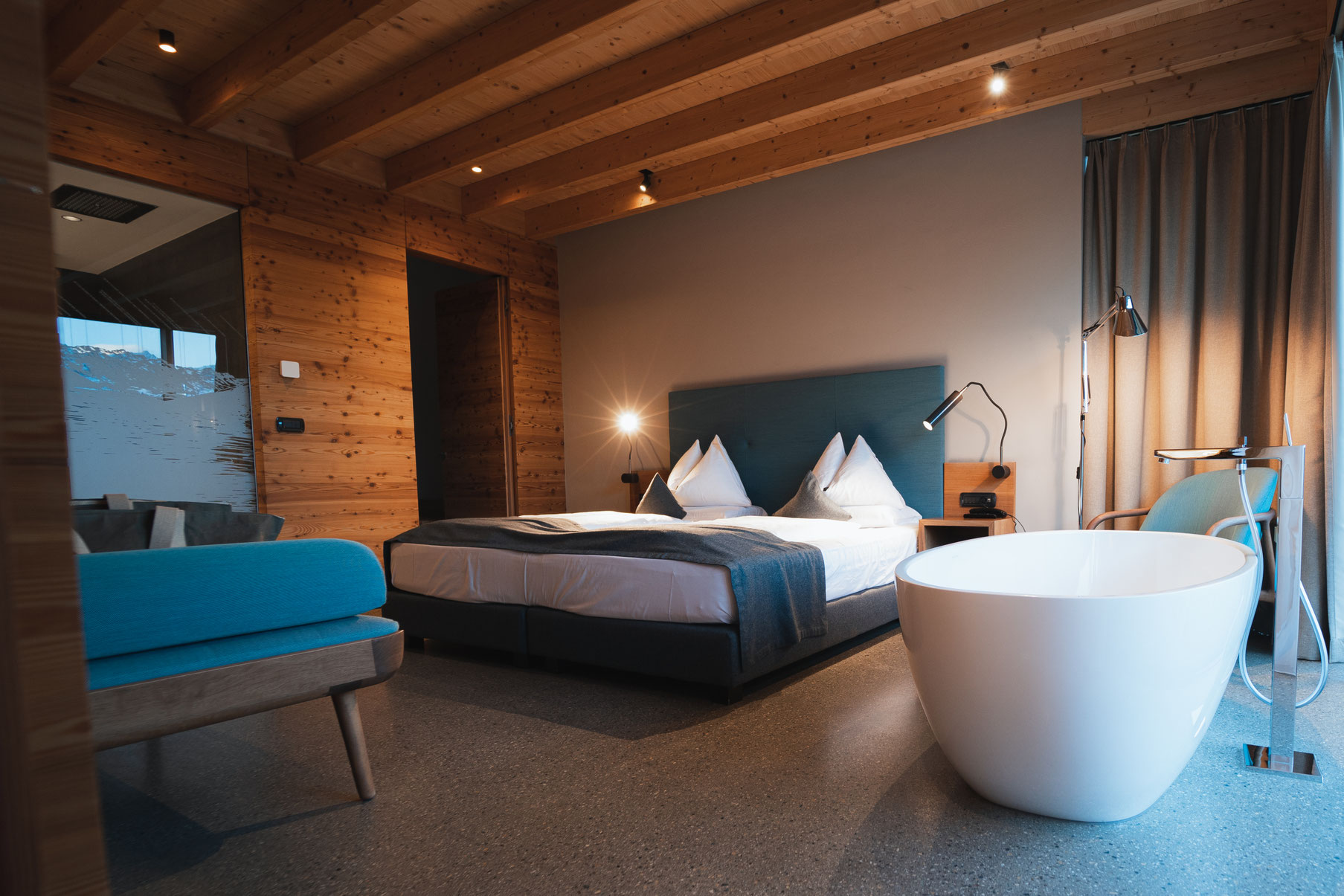 A modern suite at the Garberhof featuring a freestanding bathtub, warm wooden features and a stylish sleeping area.