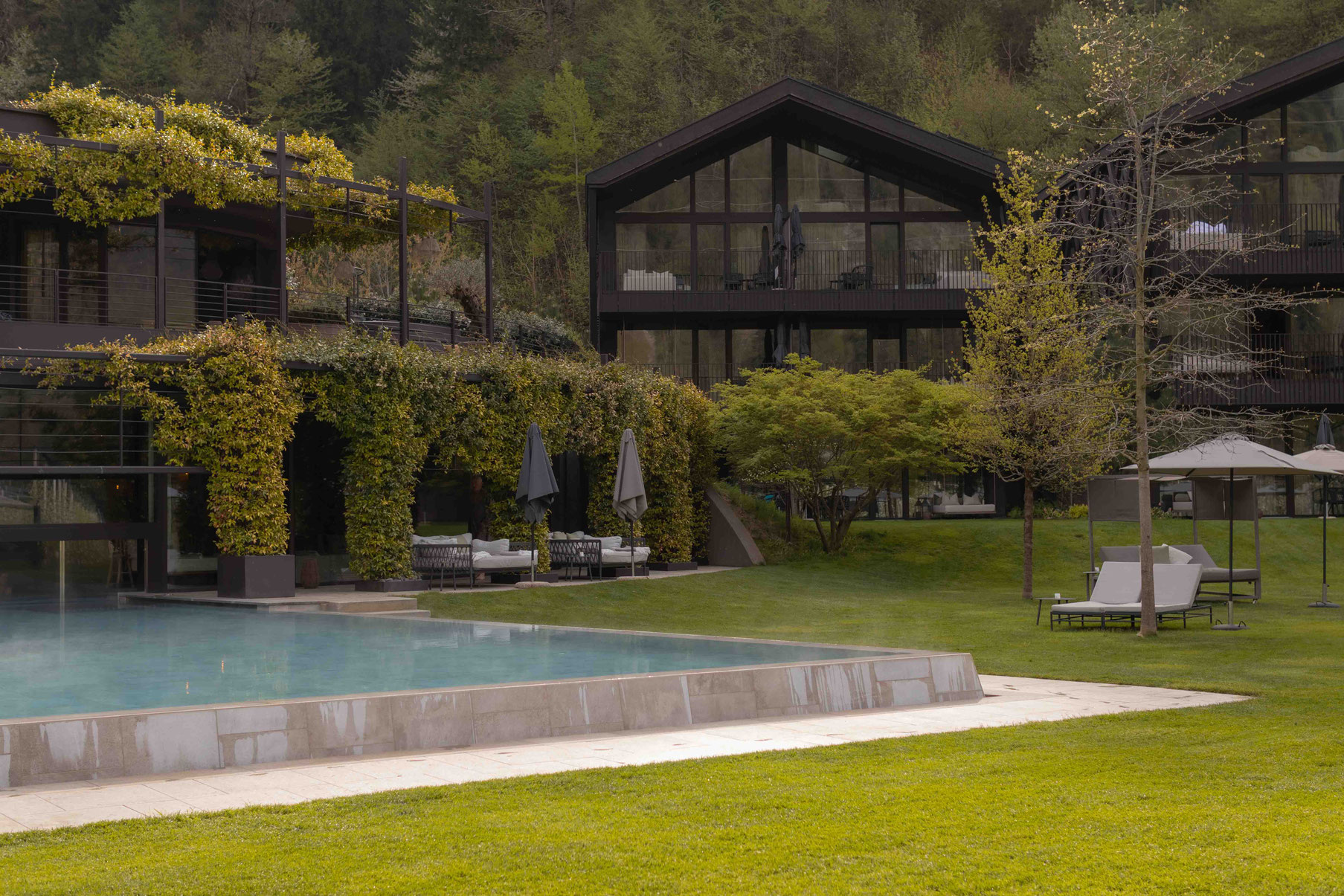 Moderner Außenbereich des Apfelhotels mit Pool, großzügiger Gartenlandschaft und begrünten Gebäuden vor bewaldeter Kulisse.