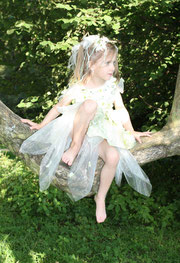 Ein Mädchen in einem Blumenkleid sitz in einem Baum vielleicht ist es auch eine kleine Fee oder Elfe mit Blumen und Bändern im Haar