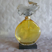 Parure verre teinté - 100 ml - "Parure" (1975) Flacon en verre incolore pressé moulé de section ovale, sa panse en forme de gourde plate facettée, disposé sur socle en résine moulée, titré, col titré sur fond laqué or, coiffé de son bouchon "vague" en ver
