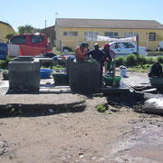 Waeschewaschende Menschen an der zentralen Wasserstelle der vierten Kategorie im Township Langa bei Kapstadt