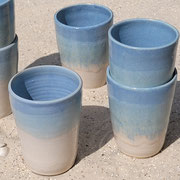mehrere teils ineinander gestapelte Becher, unten beige, oben graublau, im Sand stehend