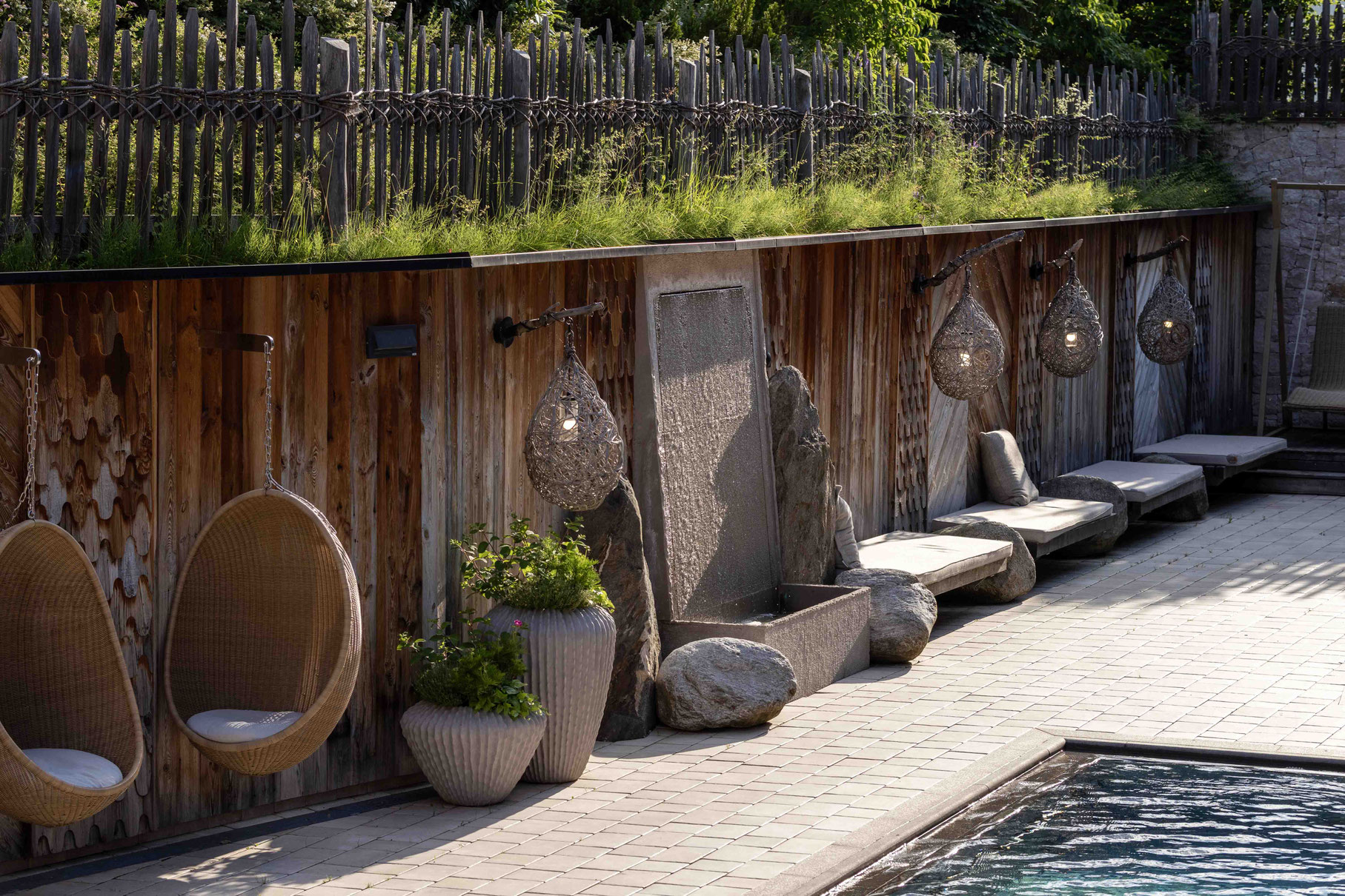 Stilvoll gestalteter Außenbereich des Pure Organic Spa im DER ENGEL im Tannheimertal mit Naturpool, Ruheliegen, Wasserwand und geflochtenen Hängesesseln. Natürliche Materialien und warme Akzente schaffen eine entspannte Wellnessatmosphäre unter freiem Him