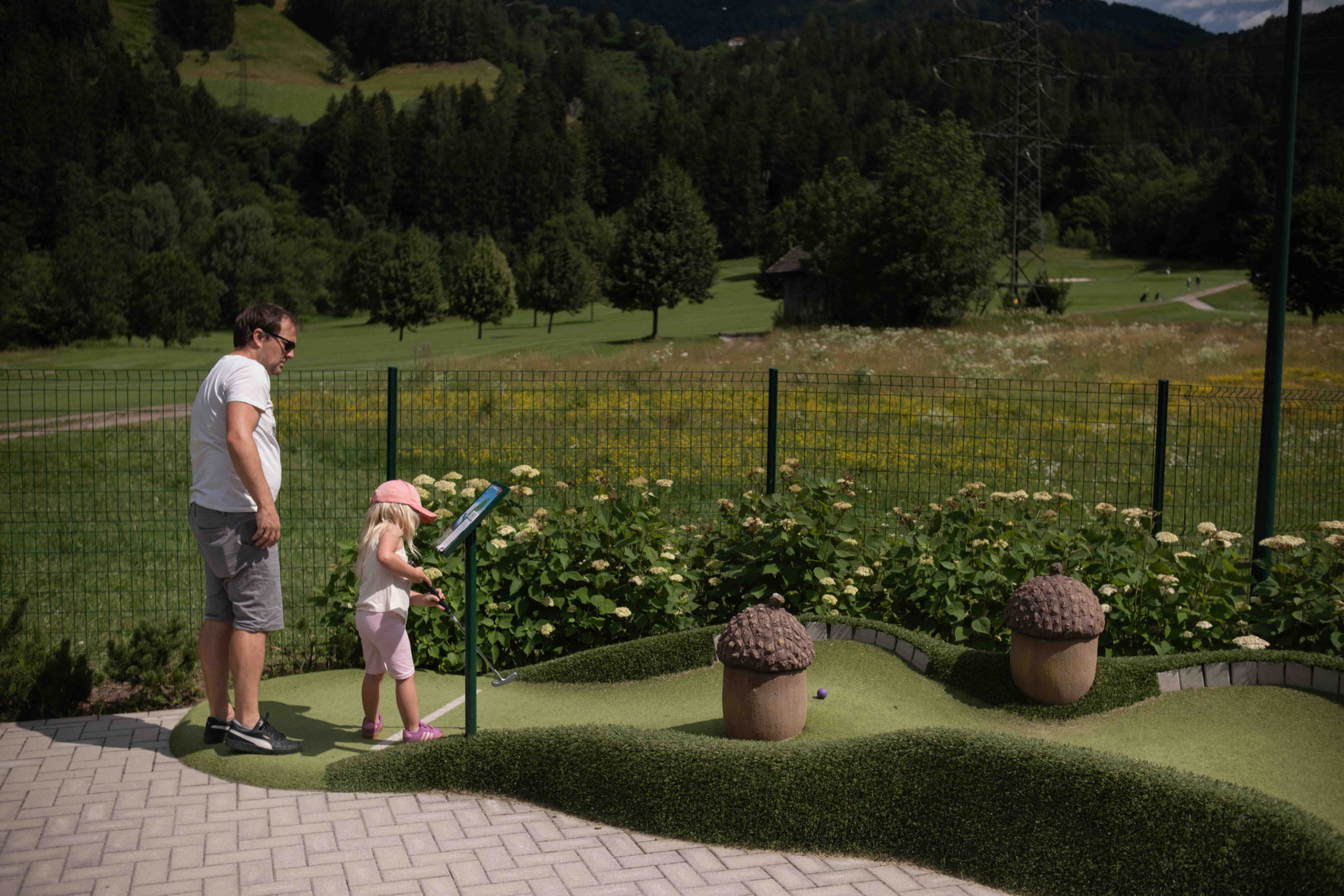 Familie spielt Minigolf auf der Abenteuer-Minigolfanlage des OBERFORSTHOFS mit Blick auf die umliegende Berglandschaft in St. Johann im Pongau, Salzburg.
