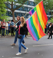 Eine Frau und ein Mann tragen jeweils eine Regenbogenfahne beim CSD Berlin. Foto: Helga Karl
