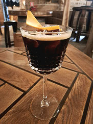 Dark cocktail with ice and orange rind in glass with stem