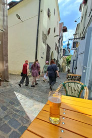 Pint of beer on wooden table with view of Old Riga buildings and walking tourists