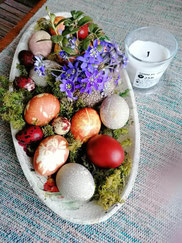 A plate of red and brown Latvian painted Easter eggs with a purple flower and a white candle