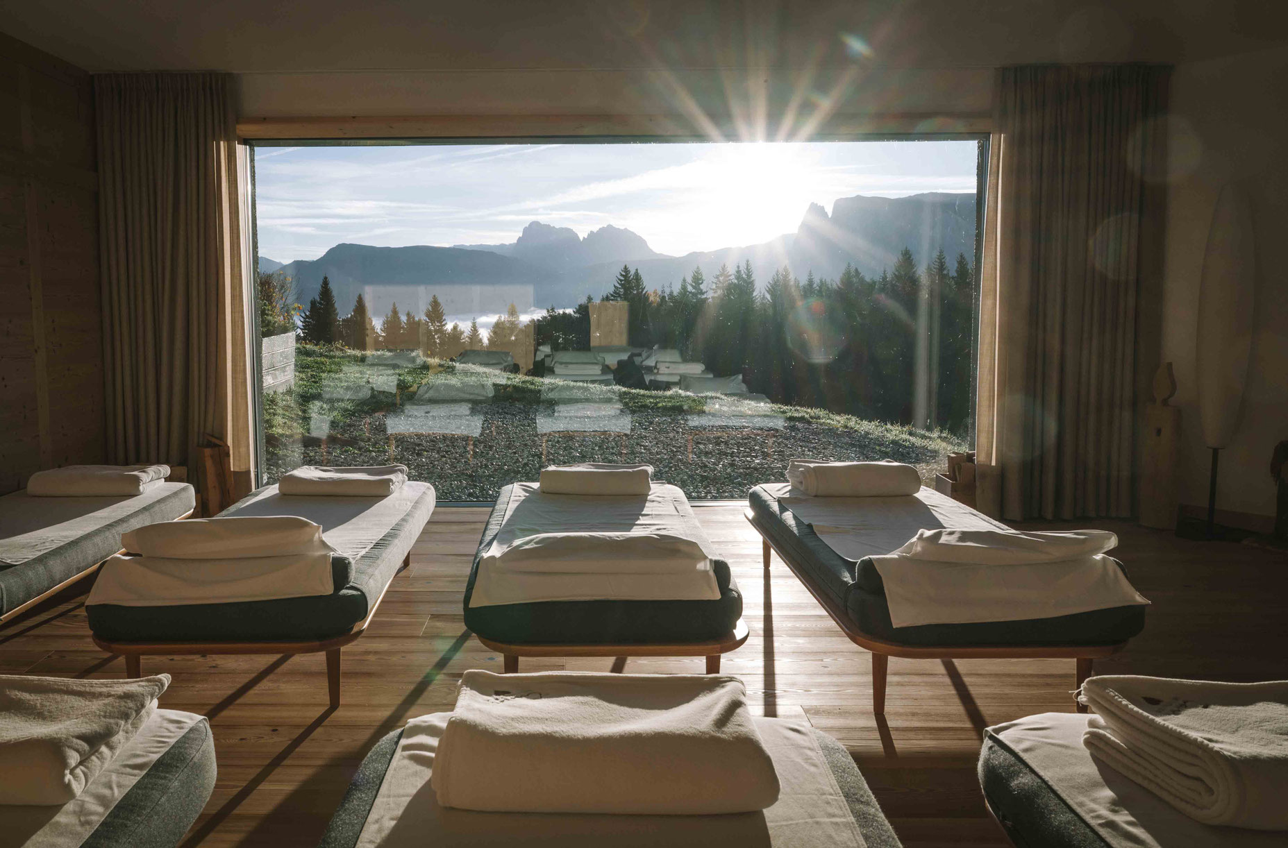 Ruheraum im Hotel Tann am Ritten in Südtirol mit großen Fenstern, Blick auf die Dolomiten und einfallendem Sonnenlicht.