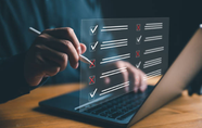 alt="Mann am Schreibtisch klickt sich durch eine digitale Checkliste durch auf seinem Laptop"
