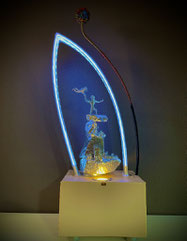 Skulptur ATARAXIE von FLoYd mit weiß-goldener LED-Beleuchtung, Drahtfiguren auf Sandstein, eingefasst von Plexiglasbogen mit Farbwechsel.