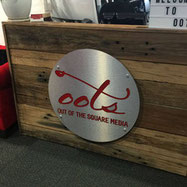 Front desk at Out of the Square Media showing logo on timber paneling