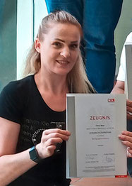Flore Musa hält stolz ihr Lehrabschlusszeugnis im Beruf Reinigungstechnik hoch und lächelt in die Kamera