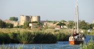 Sehenswürdigkeiten Aigues-Mortes: Segelschiff auf dem Kanal vor den historischen Stadtmauern der Altstadt von Aigues-Mortes.