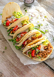 Gefüllte Tacos mit Tellerlinsen, Avocadopüree, Kirschtomaten, roten Zwiebelringen und Joghurt – bunt angerichtet von oben