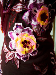 Sur l'image, une photo rapprochée d'un tissu bordeaux en dentelle avec broderie de grandes fleurs en bordeaux, rose, jaune et blanc.