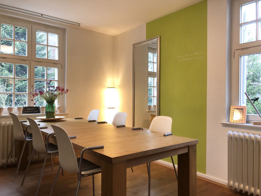 Raum mit großem Holztisch und 8 Stühlen, gemütlich eingerichtet. Ein großer Spiegel an der Wand und Spraßenfenster.