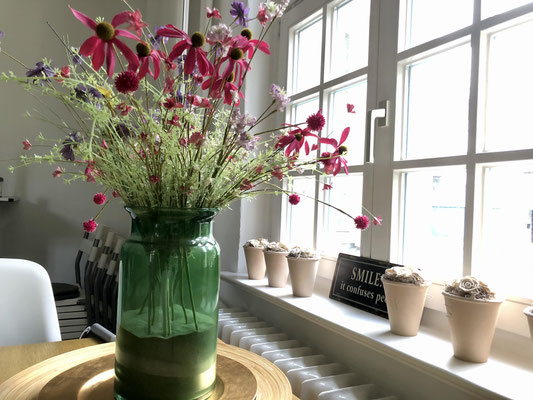 Dekorativer Blumenstraß vor einem Sprossenfenster auf dem Holztisch.