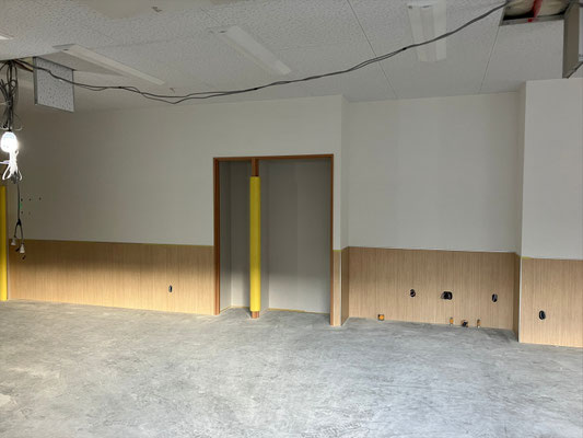 ⑨ 多目的ホール（収納庫） ： 腰壁仕上げが完了し、収納庫まわりの施工が進む多目的ホール内部。