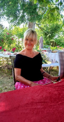 Regina sitzt im Sommergarten, feiert ihren 61. Geburtstag und trägt ein hübsches Kleid