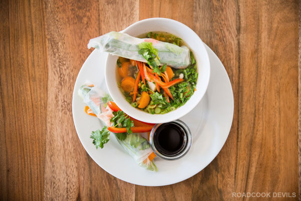 Weiße Rolle mit Ingwer, Salat, Gurken, Karotten, Paprika & frischen Gartenkräutern an einer vegetarischen Gemüsesuppe