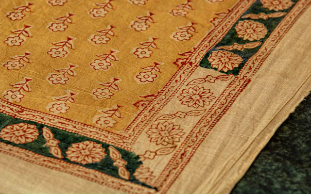Le motif floral ainsi que les frises qui encadrent la nappe ont déjà été imprimés à l’aide d’un premier tampon de bois. Il reste maintenant à appliquer le remplissage vert à l’aide d’un second tampon.