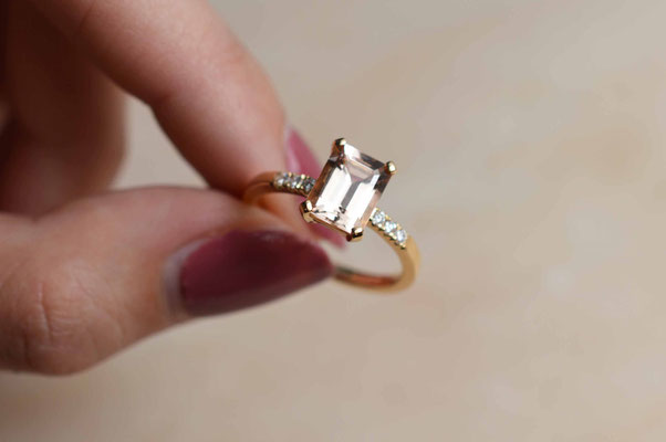 bague en or rose sertie d'une morganite et de petits diamants portée par des doigts de femme
