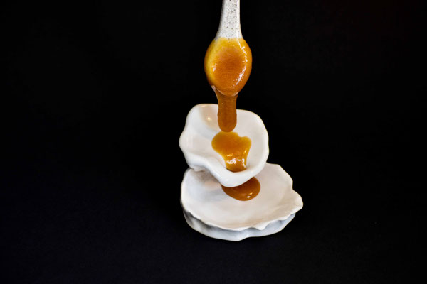 Photo d'un présentoir artistique en cérmique blanc dans le quel du Miel de Manuka de Nouvelle-Zélande est en train de couler 