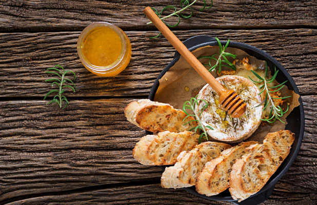 Assiette creuse de avec des tartines de pain qui sont passées au grille pain avec une cuillère en bois qui contient du Miel de Manuka, il y a un pot de 240g de Miel