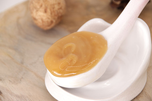 Cuillère blanche en céramique dans laquelle se trouve du Miel de Manuka de Nouvelle-Zélandeà côté d'une noix sur un plateau en bois