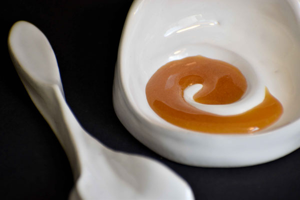 Jolie photo d'un présentoir dans le quel se trouve du Miel de Manuka de Nouvelle-Zélande avec une cuillère en céramique blanche pour une dégustation